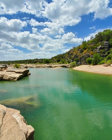 Vivid turquoise Hill Country river pool surrounded by limestone boulders and lush green trees