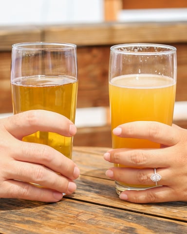 Two people clinking craft beer glasses at an outdoor brewery table