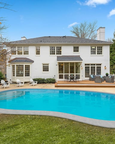 Classic white colonial home with freeform pool, green lawn, and deck