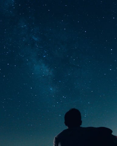 Two silhouettes sitting together under a vast Milky Way sky over Texas trees
