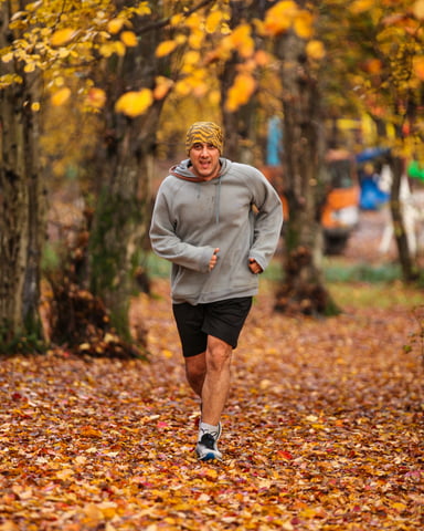 Runner sprinting through a carpet of orange and yellow fall leaves under autumn trees