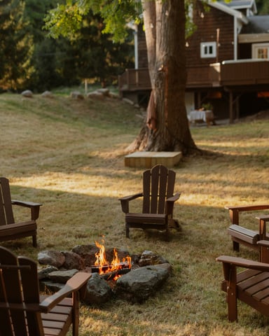 Adirondack chairs circled around a stone fire pit in a cabin backyard at golden hour