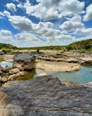 Turquoise Texas swimming hole with dramatic limestone boulders and vivid cloudy sky