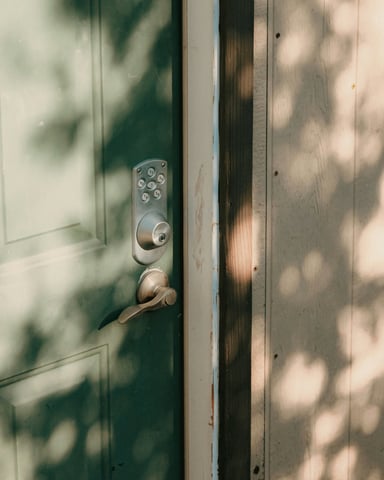 Smart keypad lock on a sage green door with dappled tree shadows