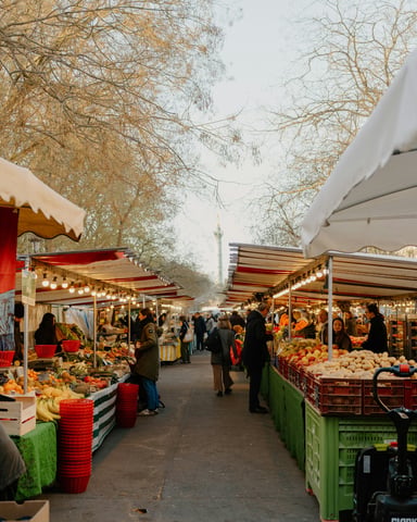 Outdoor market lane with colorful produce stalls under bare trees and warm lights