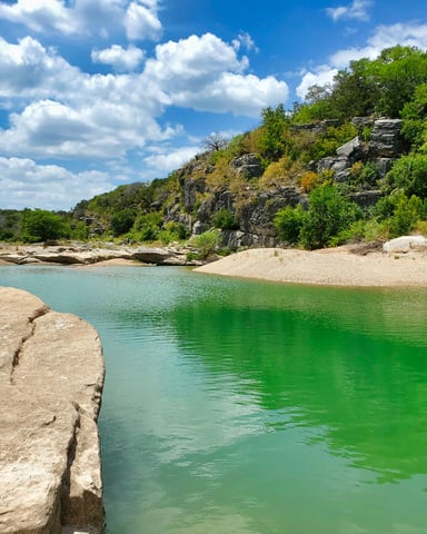 Emerald green Hill Country swimming hole with limestone cliffs and sandy beach