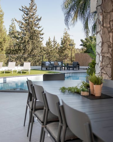 Outdoor dining table beside a pool with tall pines and stone walls