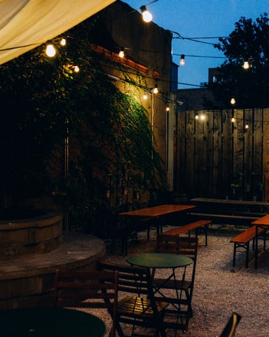 String lights glowing over a private outdoor patio at dusk with wood fence and lush greenery