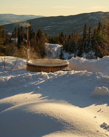 Steaming wooden hot tub at golden hour with snow-covered mountain forest behind it