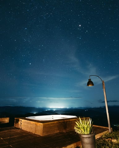 Cedar hot tub on a wooden deck under a vast starry night sky with city glow on the horizon
