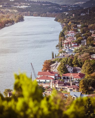 Aerial view of Lake Austin winding through green hills with lakeside homes and autumn trees