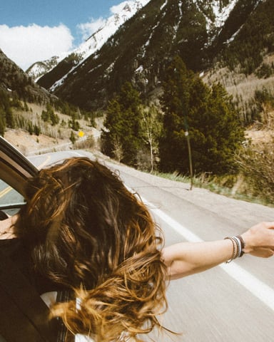 Woman leaning out a car window on a mountain road