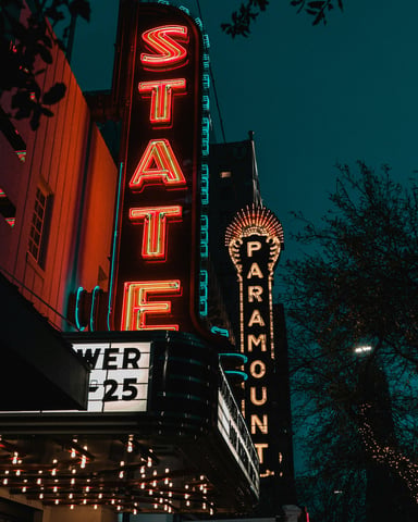 Austin State and Paramount Theater neon marquee signs glowing red at night with holiday lights in the trees