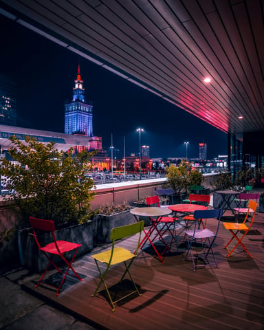 Rooftop bar with colorful chairs and tables overlooking a lit-up city tower at night