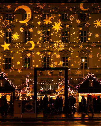 Golden stars and moons projected on a building facade with festive market stalls below