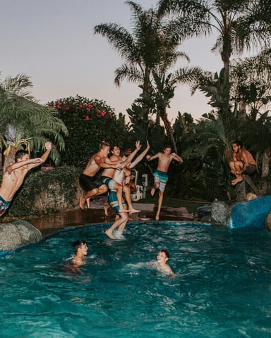 Group jumping into a tropical pool at dusk