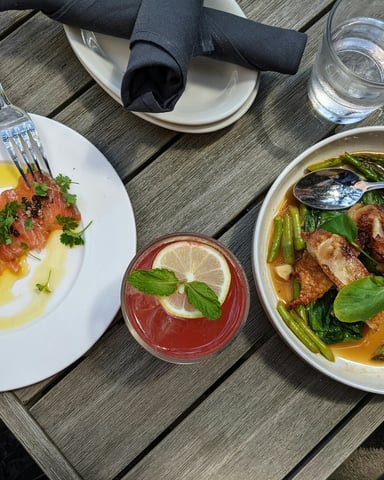 Two colorful plates of food and a cocktail on an outdoor wooden table