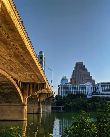 Looking up at the Congress Avenue Bridge with the Frost Tower and Austin skyline behind it under a vivid blue sky