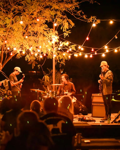 Band playing under string lights and glowing trees at an outdoor Austin venue at night