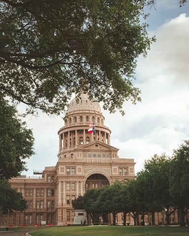 Texas State Capitol dome framed by live oak trees under a cloudy sky
