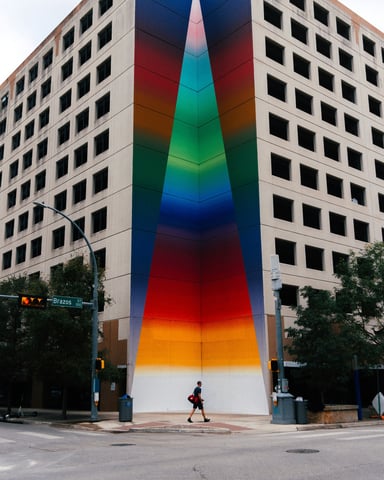 Pedestrian walking past a bold rainbow mural on a building in Austin, Texas