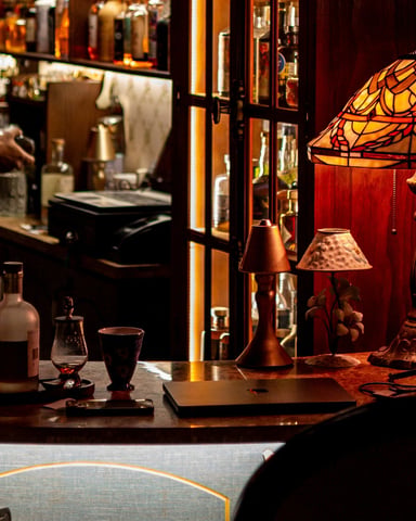 Warm moody bar interior with Tiffany lamp, rich wood tones, and bartender in background