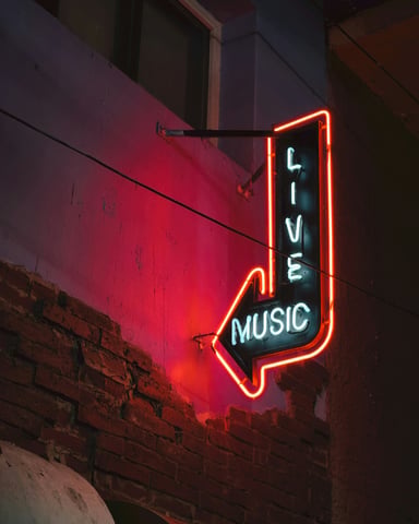 Neon Live Music arrow sign glowing red on a brick wall at night