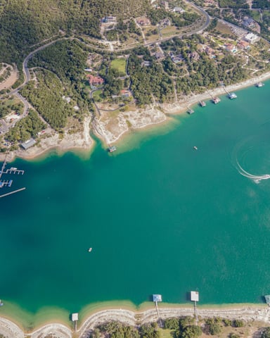 Aerial view of Lake Travis with turquoise water, boat docks, and green hillside shoreline