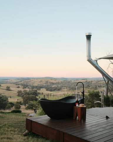 Black outdoor soaking tub on a wooden deck overlooking rolling hills at dusk