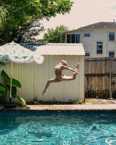 Person leaping into a backyard pool on a sunny summer day