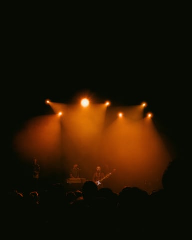 Band performing on stage under warm orange spotlights with a crowd in the foreground