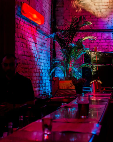 Neon-lit bar with live bassist and BEAT sign on exposed brick wall