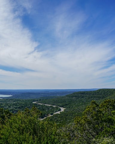 Wide panoramic view from a Hill Country hilltop with a river winding through green cedar valleys