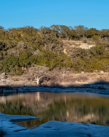 Texas Hill Country creek reflecting bare winter trees under a crisp blue sky