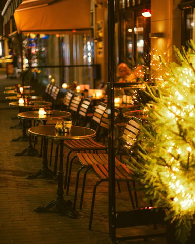 Warm outdoor restaurant patio with string lights and a lit Christmas tree on a winter evening