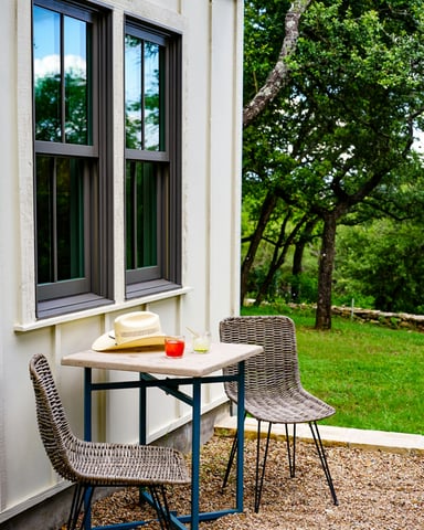 Outdoor bistro table with drinks and a straw hat, lush live oak trees and green Hill Country lawn behind
