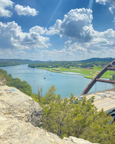 View from the 360 Overlook above Pennybacker Bridge with Lake Travis, boats on the water, and Austin skyline in the distance