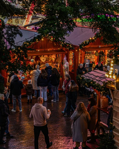 Festive Christmas market stalls with string lights and crowds of shoppers at dusk