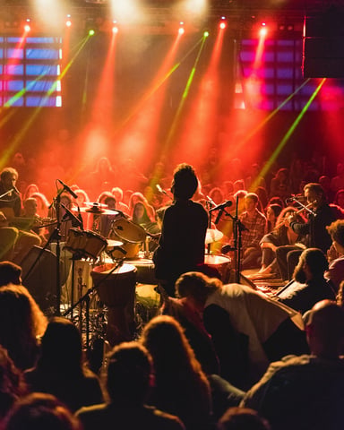 Packed indoor concert with red and orange stage lights and a full crowd