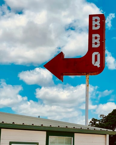 Classic red BBQ arrow sign against a bright blue Texas sky