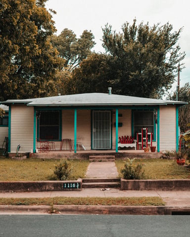 A real Austin bungalow with teal porch columns, red Adirondack chairs, and lush trees