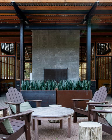 Outdoor patio with Adirondack chairs around a concrete fireplace under a timber pergola