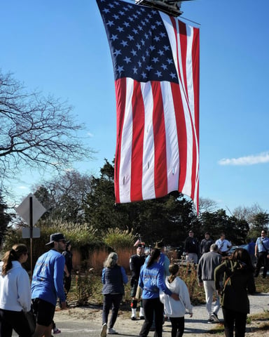 American flag hanging over a crowd of people gathered outdoors on a clear winter day