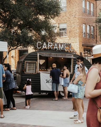 Crowd gathered around a vintage food trailer with a Caramel sign on a brick-paved Austin street