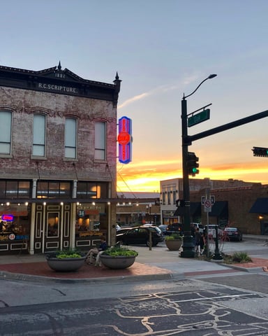Small Texas town main street corner at sunset with warm neon signs and brick storefronts