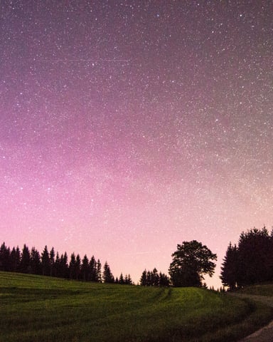 Purple and pink Milky Way sky over a winding road through green countryside