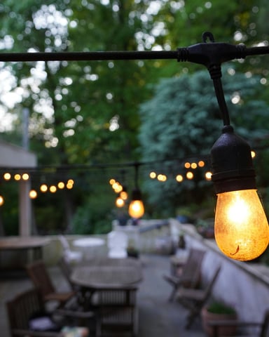 String lights glowing over a long outdoor patio at dusk with trees behind