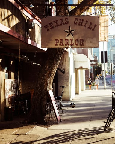 Texas Chili Parlor sign on an Austin street with warm dappled light and the city skyline behind