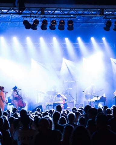 Full band performing on a lit stage with blue spotlights and a packed crowd at an outdoor festival
