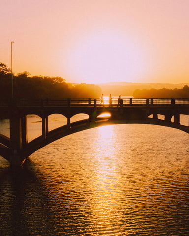 Lamar Bridge silhouetted against a golden sunset over Lady Bird Lake in Austin